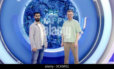 Due uomini sorridenti che mostrano i pollici in uno studio moderno. Supporto Foto Stock