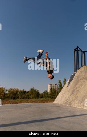 Nella fase finale di backflip freerunner scende dall'altezza dopo essere stato lanciato da una pendenza di cemento, mostrando potenza, consapevolezza aerea e urban a. Foto Stock