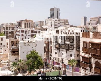 Jeddah, Arabia Saudita – 20 aprile 2025: Contrasto tra vecchi edifici con finestre in legno a al Balad Jeddah e moderni grattacieli sullo sfondo Foto Stock