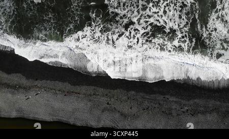 Onde che si infrangono sulla spiaggia di sabbia nera Foto Stock