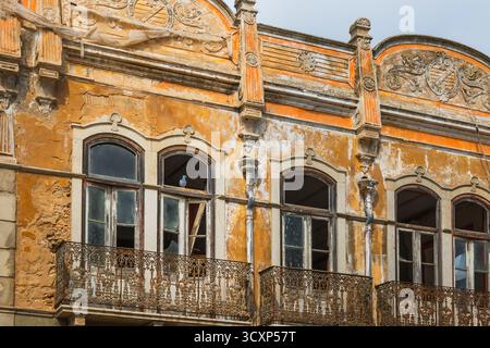 Un edificio abbandonato in Portogallo mostra pareti incrinate, balconi in ferro e dettagli architettonici sbiaditi. Foto Stock