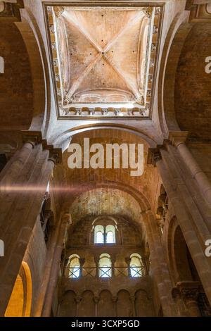 Una vista dall'angolo basso rivela gli alti archi in pietra e il soffitto a volta di una chiesa storica, con luce solare che scorre attraverso le finestre ad arco. Foto Stock