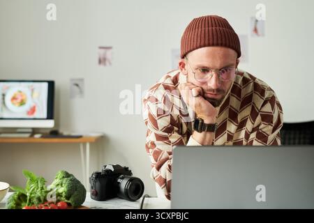 Uomo che indossa occhiali che lavora su un notebook in ufficio domestico Foto Stock