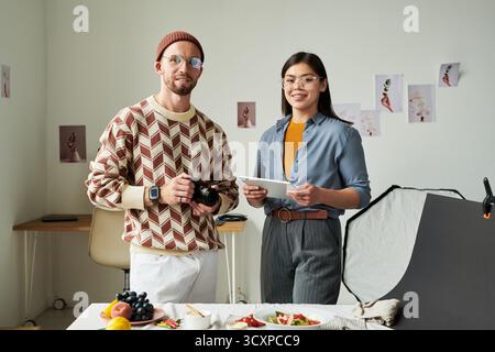 Uomo che tiene la fotocamera e donna asiatica che usa un tablet digitale Foto Stock