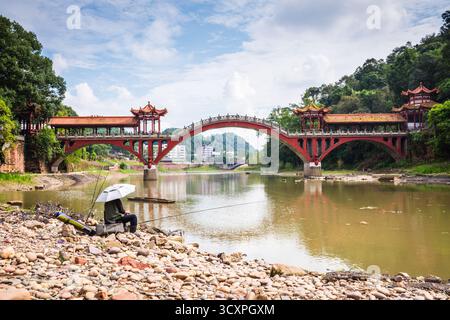 Leshan, Cina - 29 settembre 2018: Uomo che pesca sul fiume di fronte al ponte Leshan. Foto Stock