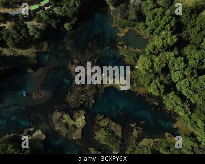 Veduta aerea di un fiume turchese vivace che si snoda attraverso una fitta foresta verde con vegetazione sommersa e piccole barche che navigano nel trasparente tranqu Foto Stock