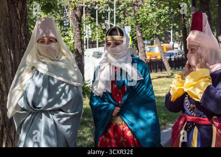 Questa immagine mostra tre donne elegantemente vestite adornate con un vivace abbigliamento tradizionale, completo di veli, mentre passeggiano attraverso un lussureggiante set del parco Foto Stock