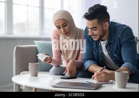 Famiglia musulmana positiva contando le proprie spende, sentendosi ricca Foto Stock