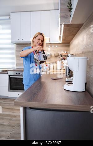 Infermiera sorridente che versa caffè in cucina durante la pausa di lavoro Foto Stock