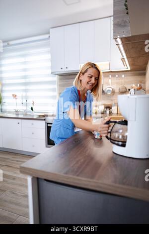 Infermiera sorridente che versa caffè in cucina durante la pausa di lavoro Foto Stock