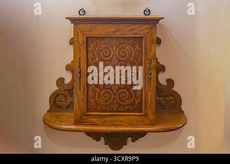 Un armadio in legno decorato con pareti beige, con intricate incisioni e un design ad arco, caratterizzato da un pannello decorativo centrale che ne esalta la Foto Stock