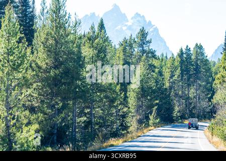 Teton Road è fiancheggiata da fitte foreste di conifere che conducono verso le maestose Teton Mountains. Un solo veicolo viaggia da solo sulla strada Foto Stock