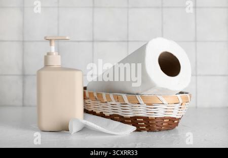Bottiglia con sapone e rotolo di asciugamani di carta su un tavolo bianco contro le pareti piastrellate Foto Stock