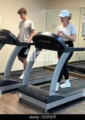 Donna con berretto bianco e adolescente che corre e cammina sul tapis roulant con sneakers bianche nella palestra sportiva Foto Stock