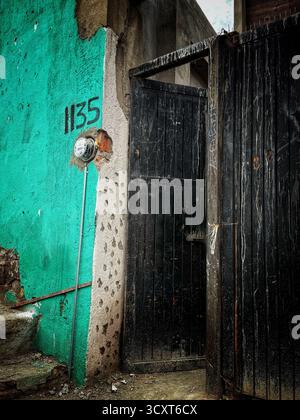 Scena urbana con una parete turchese intemprata, un cancello nero e il numero 1135 dipinto su una superficie di cemento Foto Stock