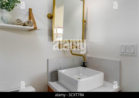 Bagno moderno con lavandino in ceramica bianca, rubinetteria in ottone oro e specchio Foto Stock