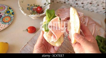 Una persona anonima prepara un panino con salsiccia, lattuga e mortadella, maionese fatta in casa in cucina. Cucina italiana, alta qualità coltivata in azienda Foto Stock