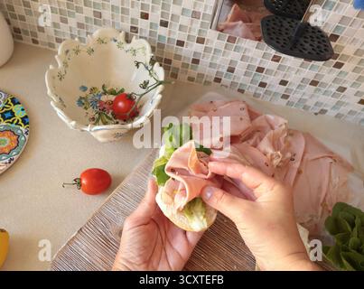 Una persona anonima prepara un panino con salsiccia, lattuga e mortadella, maionese fatta in casa in cucina. Cucina italiana, alta qualità coltivata in azienda Foto Stock