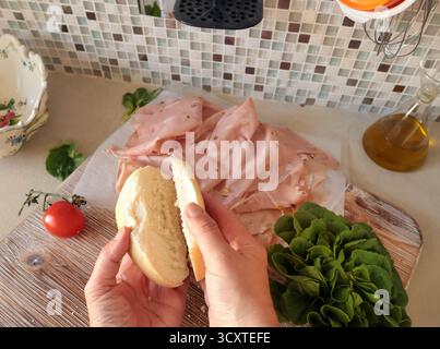 Una persona anonima prepara un panino con salsiccia, lattuga e mortadella, maionese fatta in casa in cucina. Cucina italiana, alta qualità coltivata in azienda Foto Stock