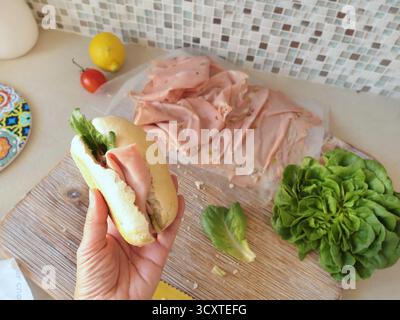 Una persona anonima prepara un panino con salsiccia, lattuga e mortadella, maionese fatta in casa in cucina. Cucina italiana, alta qualità coltivata in azienda Foto Stock