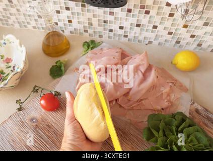 Una persona anonima prepara un panino con salsiccia, lattuga e mortadella, maionese fatta in casa in cucina. Cucina italiana, alta qualità coltivata in azienda Foto Stock
