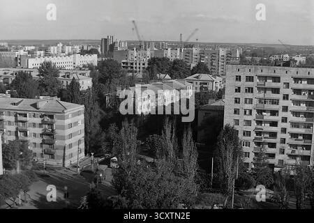 Una foto d'archivio panoramica ad alto angolo degli anni '1980 mostra il paesaggio urbano intorno a Oktyabrskoy Revolyutsii Street (ora Vasylivska Street) a Sloviansk. La vista cattura un mix di architettura di epoca sovietica, da bassi appartamenti in mattoni a nuovi edifici a pannelli. All'orizzonte, le gru a torre simboleggiano l'espansione attiva della città. Questa immagine è un prezioso documento di sviluppo urbano e della vita quotidiana di un pacifico Donbas prima della guerra Foto Stock