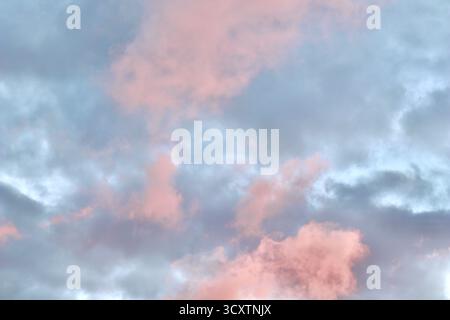 Un'atmosfera da sogno in cui una massa drammatica di nuvole di rosa e pesca si illumina contro una malva pallida e il cielo blu durante il tramonto o l'alba, riempiendosi Foto Stock