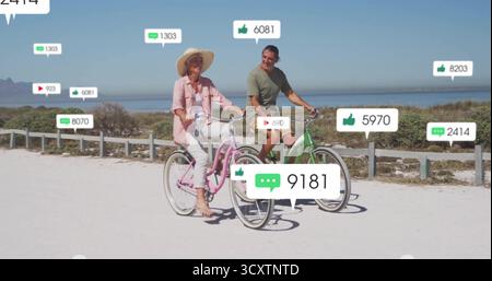 Una coppia matura pedalando su un sentiero costiero sabbioso, con icone dei social media Foto Stock