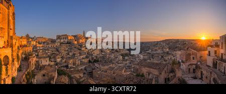 Un'ampia immagine panoramica 65x24 Xpan da una vista serena di Matera all'alba, con il sole che sorge appena sopra l'orizzonte. Le storiche case in pietra di Th Foto Stock