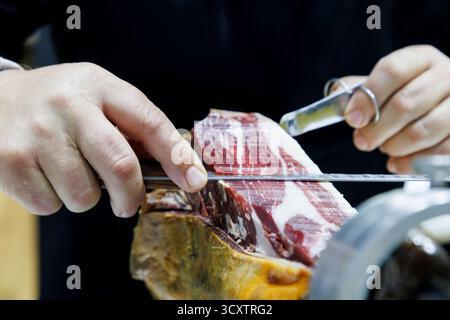 Chef professionista che affetta il prosciutto iberico presso la cucina gourmet del ristorante di lusso. tagliate delicatamente la carne affettata con coltello e pinze, mostrando il textu Foto Stock