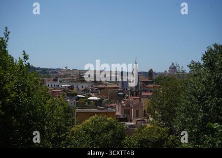 Un'ampia vista panoramica dello skyline romano incorniciato da alberi con edifici storici, la guglia di una chiesa e la cupola della basilica di San Pietro. Foto Stock