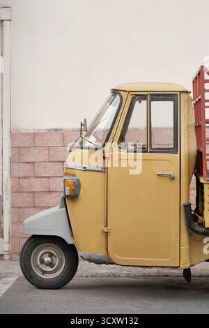 Veicolo a tre ruote giallo d'epoca parcheggiato da una parete color pastello in Italia, in stile retrò minimalista. Foto Stock