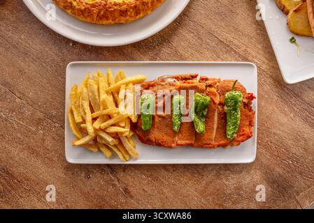 Cachopo asturiano ripieno di prosciutto Serrano e formaggio fuso, croccante e impanato dorato, accompagnato da peperoni e patatine fritte arrosto Foto Stock