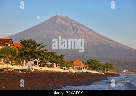Vista panoramica del vulcano del Monte Agung dalla spiaggia di Amed con la luna piena nel cielo. Amed, Karangasem Regency, Bali, Indonesia. Foto Stock