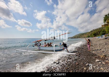 Un uomo spinge la barca con i turisti a bordo per aiutarla a navigare lontano dalla riva. Amed, Karangasem, Bali, Indonesia. Foto Stock