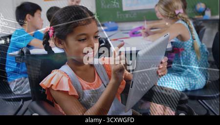 Utilizzo di una studentessa che indossa tute che interagisce con un tablet alla scrivania in classe, con sovrapposizioni matematiche Foto Stock