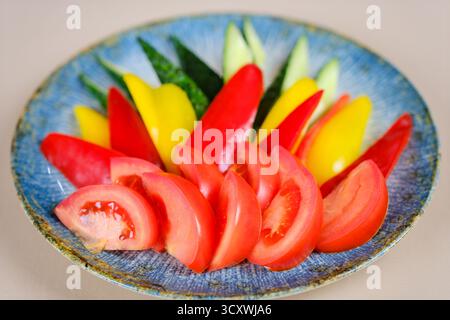 pepe, pomodoro, cetriolo in pezzi su un piatto di verdure, brocca di olio, recipiente con verdure, coltello e forchetta sul tavolo. Foto di alta qualità Foto Stock