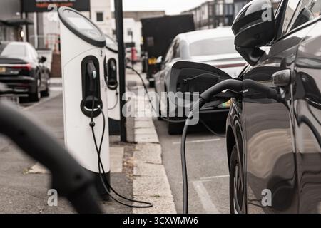 Le auto elettriche che si ricaricano su strada con un'infrastruttura di ricarica visibile Foto Stock