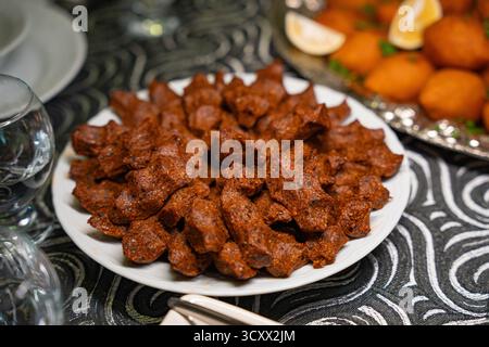 Piatto di cig kofte tradizionale servito con insalata di barbabietole, verdure e fette di limone. Kibbeh tradizionale della cucina mediorientale e turca. Bulgur piccante Foto Stock