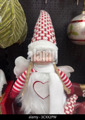 Un'incantevole bambola natalizia con guance rosate, con cappello rosso e bianco a maglia, maniche a righe e sciarpa bianca soffice con un'scintillante mela a cuore Foto Stock