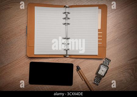 Apri organizer, uno smartphone, una penna e un orologio da polso su una scrivania di legno. Foto Stock