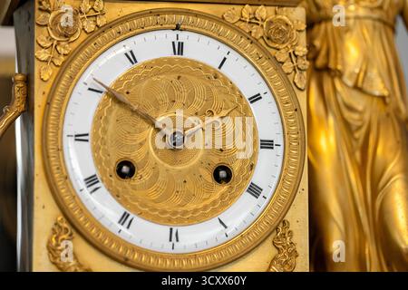 Lussuoso orologio in oro con quadrante inciso, numeri romani e bordi floreali decorati. Un raffinato centrotavola che evoca la classica maestria artigianale e tim Foto Stock
