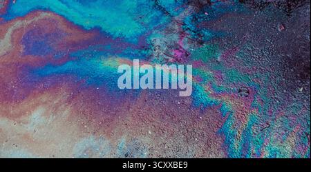 Lucentezza dell'olio che crea un vivace motivo iridescente dell'arcobaleno su asfalto scuro, che riflette la luce e illustra i concetti di inquinamento, contaminazione ed e. Foto Stock