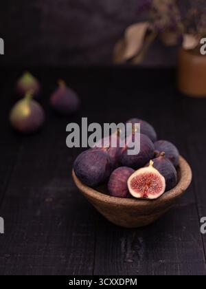 fichi tagliati a fette in una ciotola di legno circondata da fichi interi e decorazioni in vaso sul retro, stile rustico fotografico Foto Stock