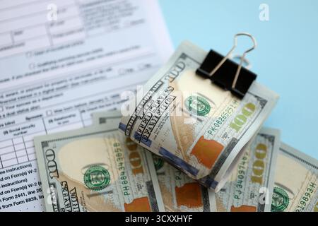 Grande quantità di banconote in dollari statunitensi sul tavolo con modulo di dichiarazione dei redditi individuale da vicino. Concetto di tassazione e contabilità negli Stati Uniti Foto Stock