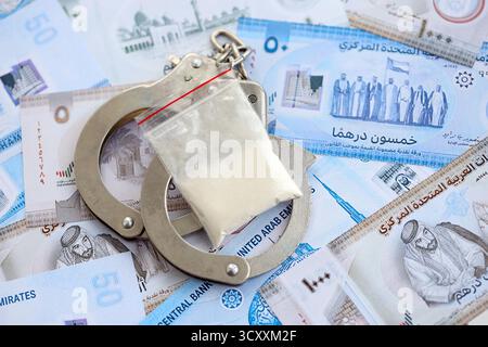 Banconote in valuta dirham degli Emirati Arabi Uniti e pacchetto di cocaina con manette da vicino. Il concetto di crimini di droga Foto Stock