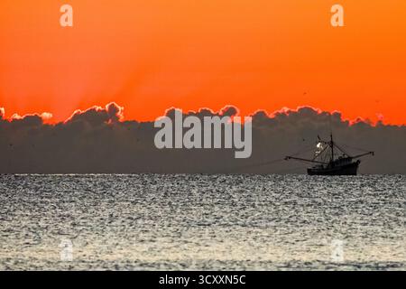 Isola di Palms, Stati Uniti. 16 ottobre 2025. Un peschereccio a strascico di gamberi trascina la costa mentre il sole inizia a salire su una bassa riva di nuvole sull'Oceano Atlantico lungo Front Beach, il 16 ottobre 2025 a Isle of Palms, South Carolina. Crediti: Richard Ellis/Richard Ellis/Alamy Live News Foto Stock