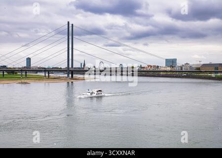 Barca turistica in barca a vela sotto il ponte strallato sul fiume Reno con skyline della città e ruota panoramica nell'autunno nuvoloso Düsseldorf Germania Foto Stock