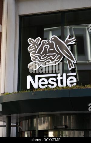 Primo piano del logo Nestlé e dell'icona del nido montati vicino all'ingresso della porta girevole in vetro dell'edificio degli uffici dell'azienda. Amstelveen, Paesi Bassi. 28 Foto Stock