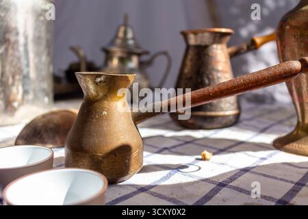 Un'antica collezione di tazze e pentole da caffè turche tradizionali su una disposizione STILL Life di tovaglia a scacchi Foto Stock